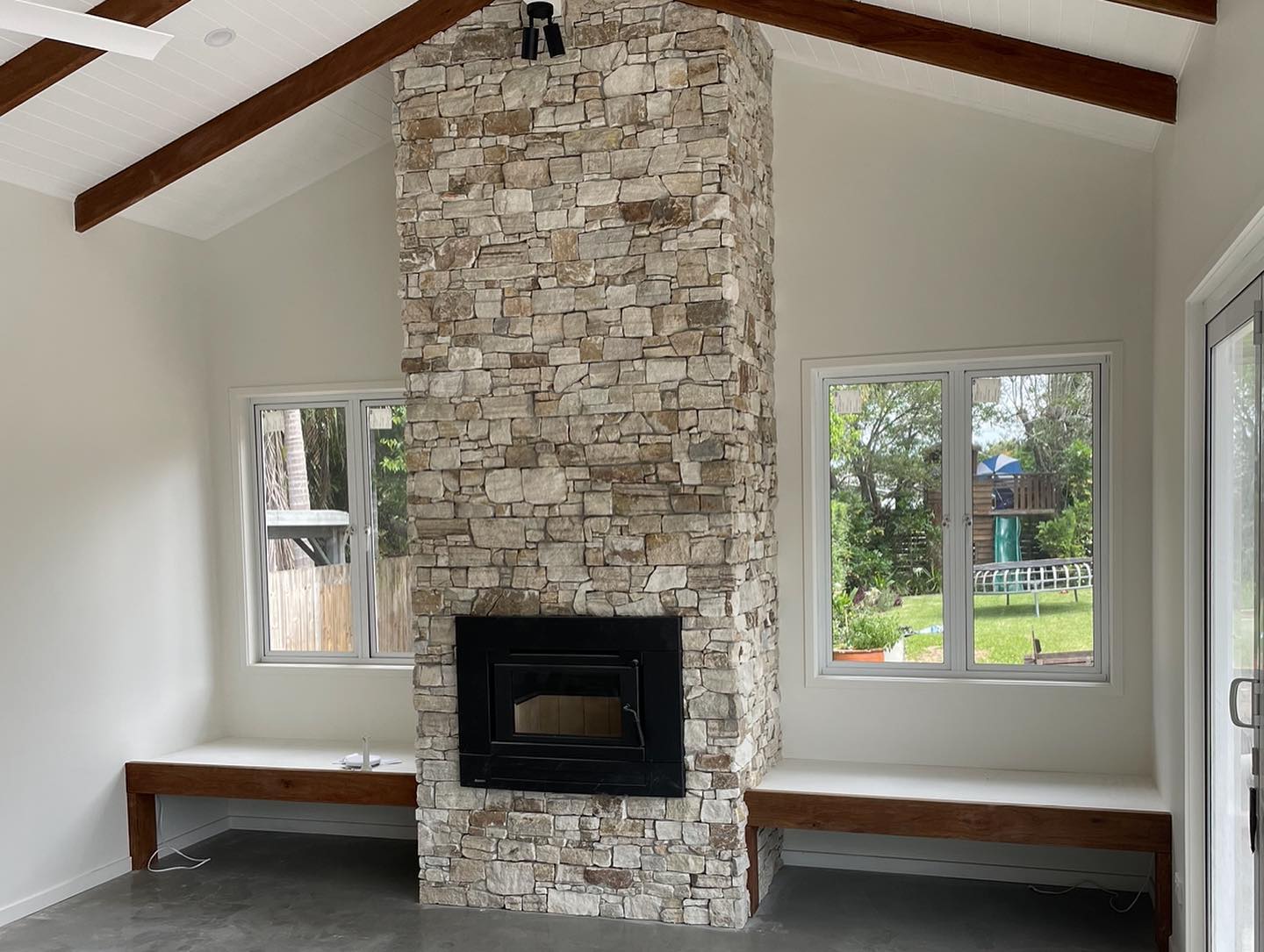 Stone Fireplace Feature Wall: Floor-to-ceiling stone fireplace with a built-in wood heater and timber bench seating.
